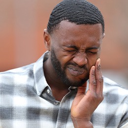 Man in collared shirt rubbing jaw in pain