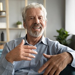 A mature man sitting on a couch and talking with someone