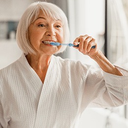 Senior woman in bathrobe brushing her teeth