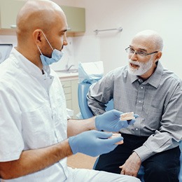 A dentist showing model dentures to an older man