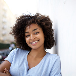 Woman in light blue shirt leaning against wall smiling