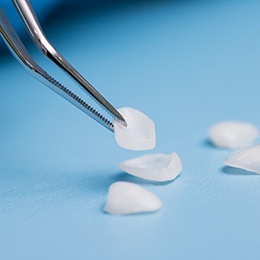 Tweezers holding a veneer while several veneers sit nearby