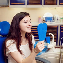 A dental patient admiring her treated smile with a hand mirror