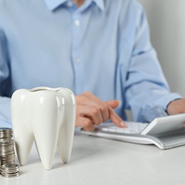 A patient using a calculator next to a model tooth and stacks of coins