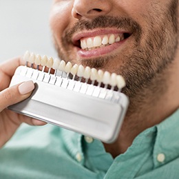 A happy, smiling man brushing his teeth in front of a bathroom mirror