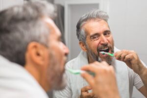 Older man brushing his teeth in front of bathroom mirror