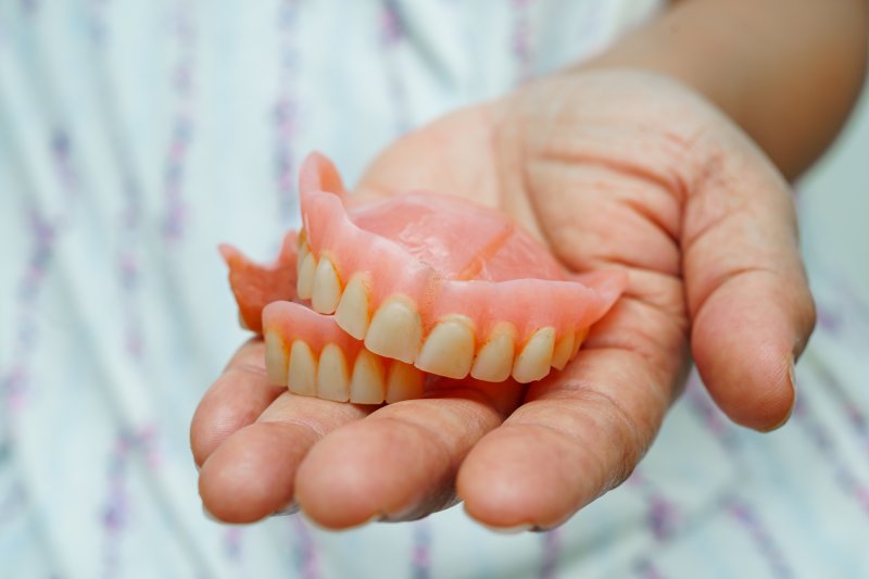 A hand holding worn out dentures
