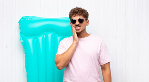Young man with floatie and sunglasses suffering from tooth pain